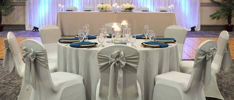 A round table with white chairs, each with a bow on the backrest, set for a formal event.