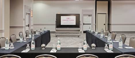 A conference room with a long table, chairs, water bottles, and a screen displaying 'Crowne Plaza.'