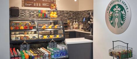 L’intérieur d’un café, avec un tableau affichant le menu, un présentoir de pâtisseries et un réfrigérateur pour les boissons.