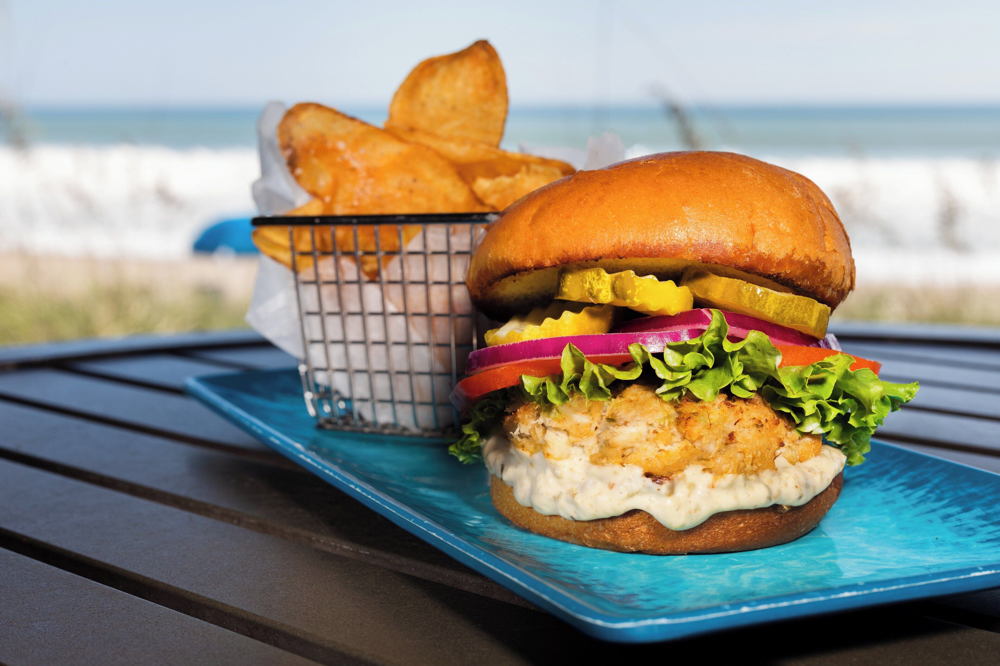 A sandwich with a bun, lettuce, tomato, and pickles, accompanied by a basket of chips, on a blue plate.