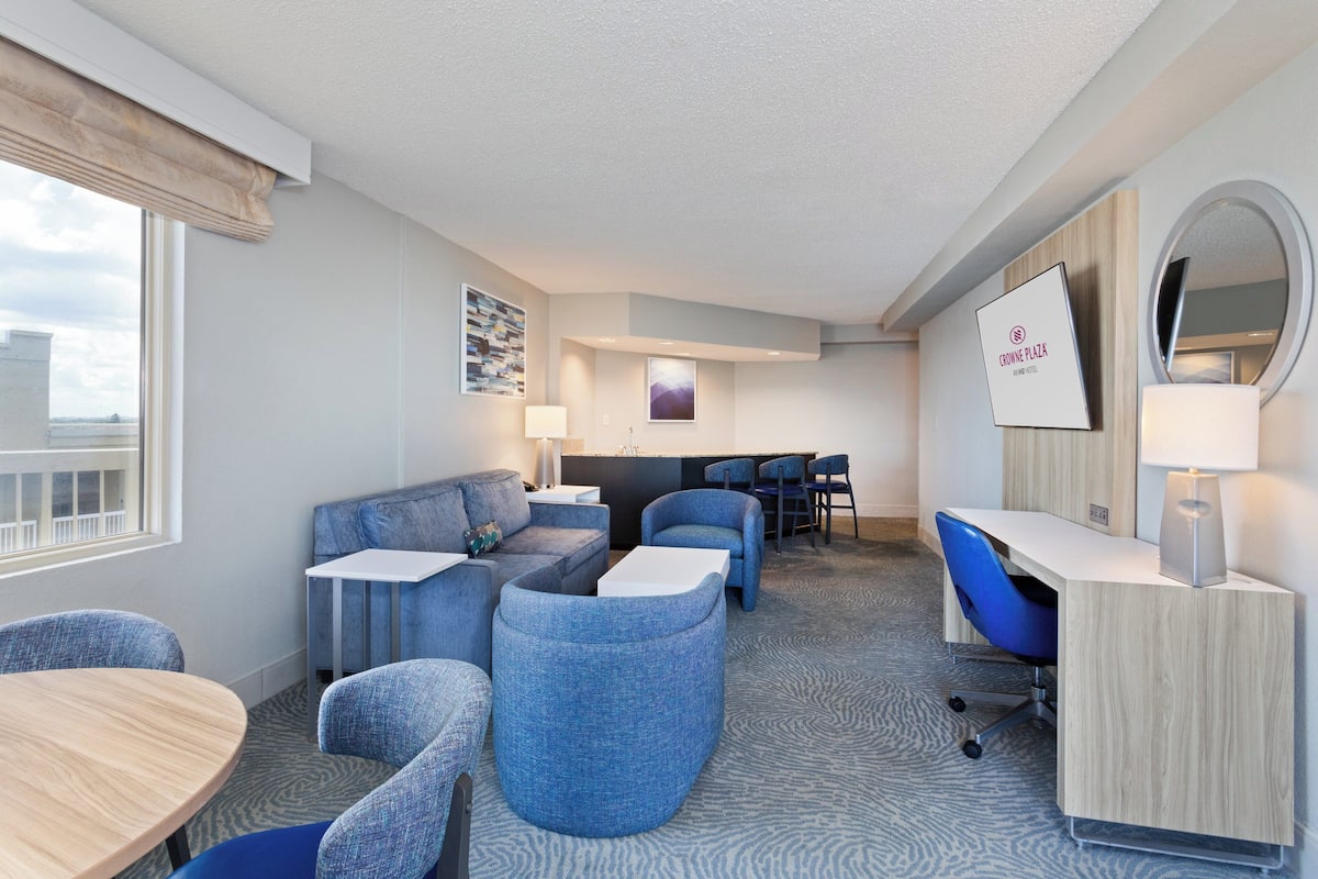 A hotel room with a seating area, a desk, and a large mirror.