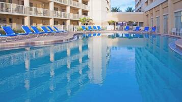A swimming pool with blue lounge chairs, a white fence, and a building with balconies in the background.