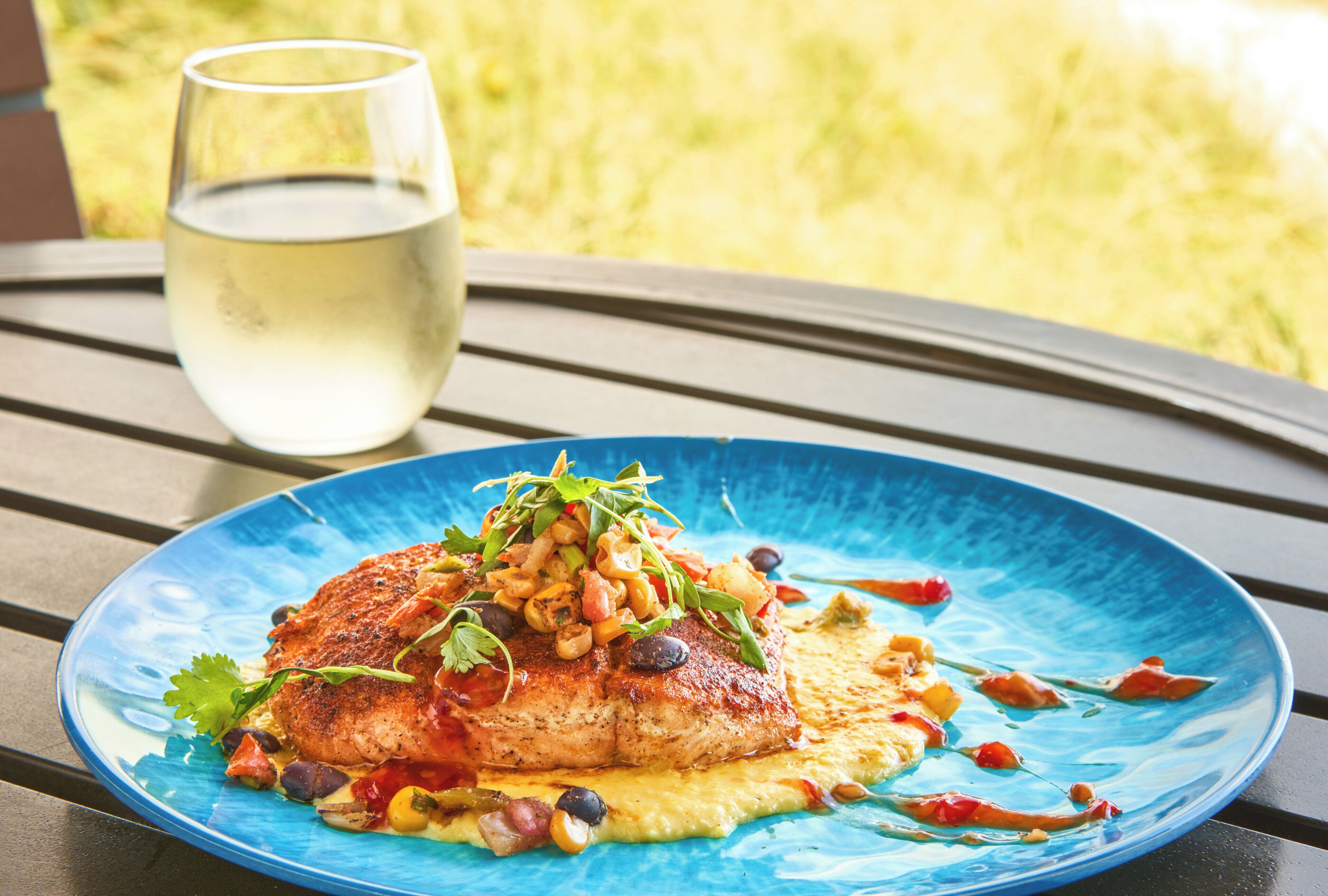 A blue plate with a grilled chicken dish, garnished with herbs, on a wooden table.