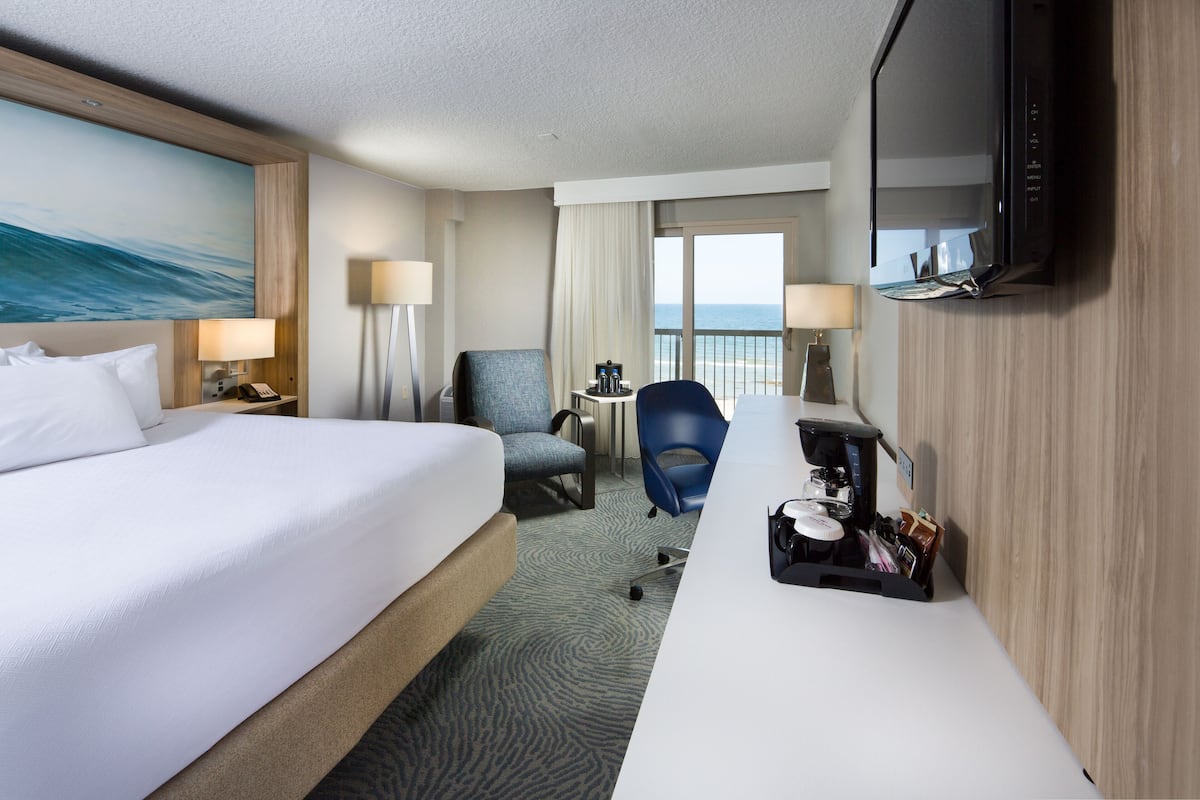 A hotel room with a bed, a desk with a coffee maker, a chair, and a TV.