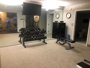 A gym with exercise equipment, a television, clocks, and a mirror. - Crowne Plaza Melbourne - Oceanfront by IHG (Indialantic)