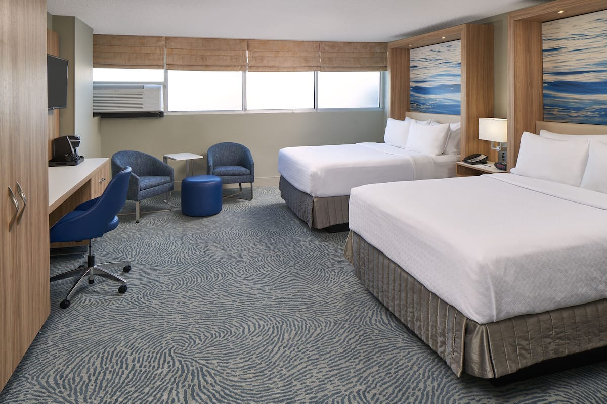 A hotel room with two beds, a desk, a chair, a small table, and a lamp.