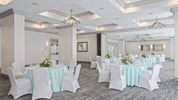 Un salón de conferencias con mesas redondas, sillas blancas y piso alfombrado.