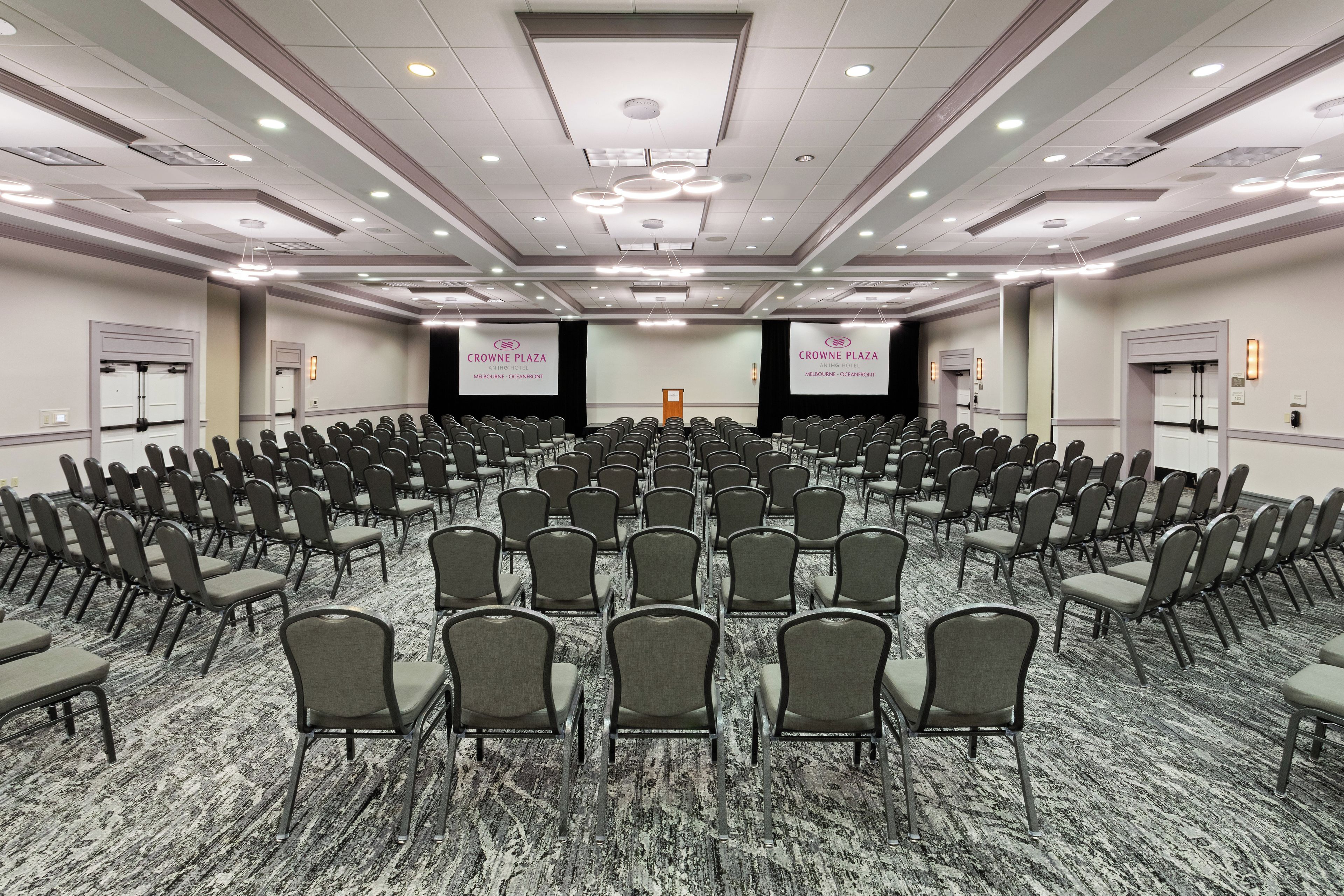 Une salle de conférence avec des rangées de chaises, une scène et des banderoles.