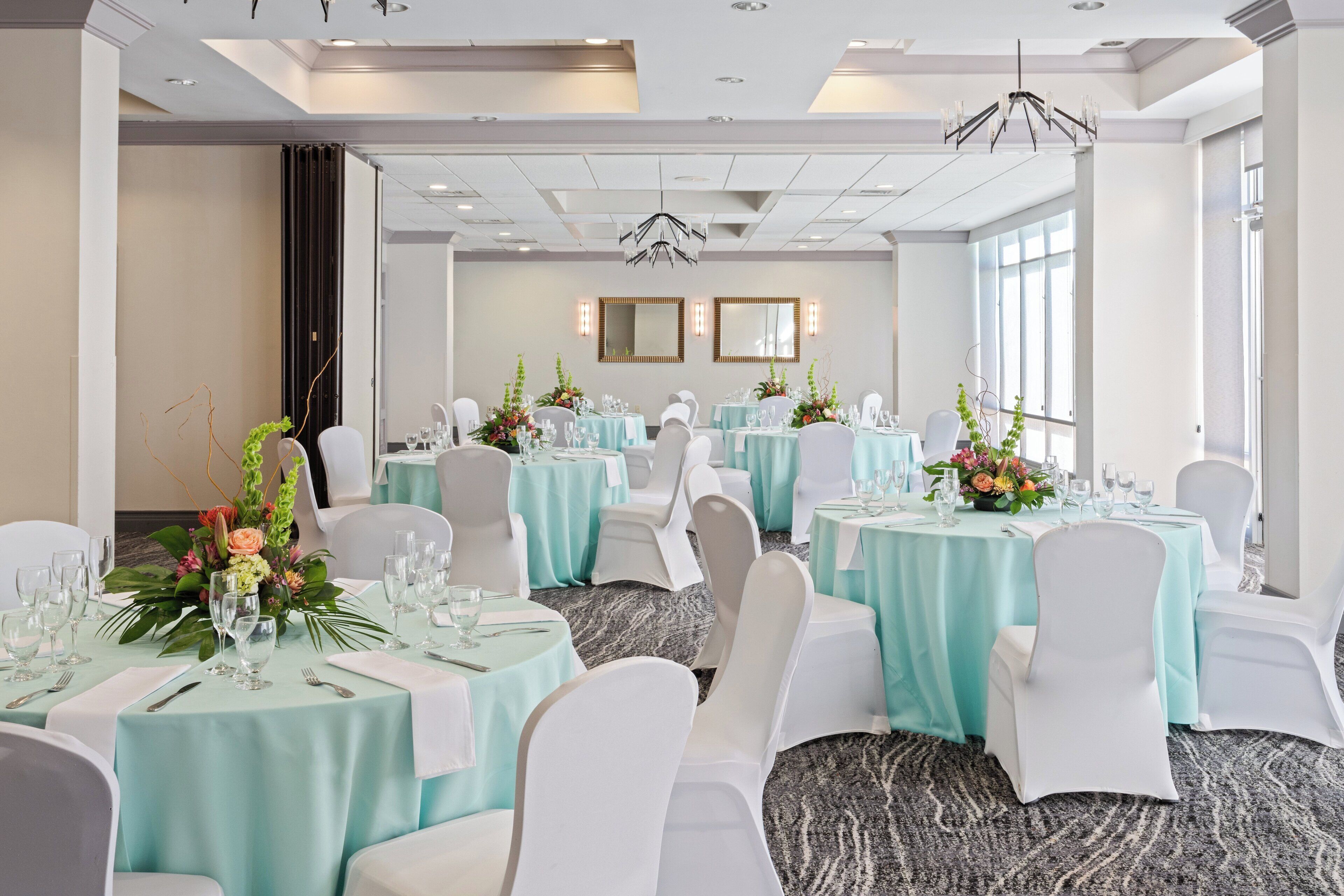 A banquet hall with round tables, white chairs, and light blue tablecloths.