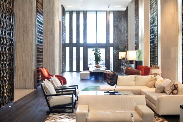 A spacious lobby with a modern design, featuring a seating area with sofas and chairs, a coffee table, and a decorative plant.