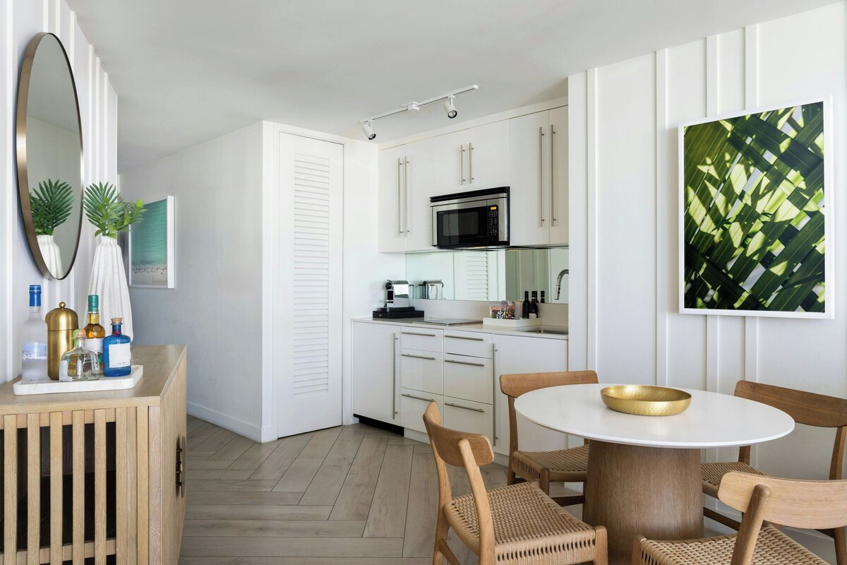 A modern kitchen with white cabinetry, a microwave, and a dining area with a round table and wicker chairs.
