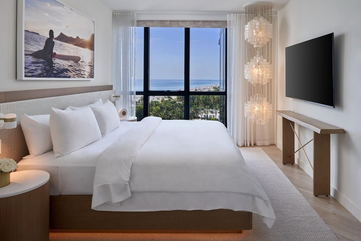 Une chambre d’hôtel moderne dotée d’un grand lit, d’une télévision, d’une vue sur l’océan et d’un lustre.