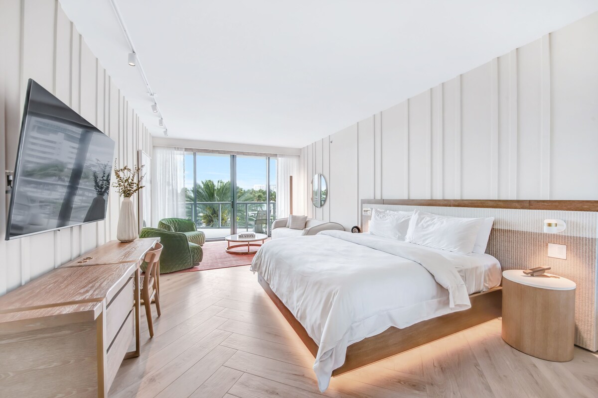 A modern bedroom with a large bed, a desk, and a TV.
