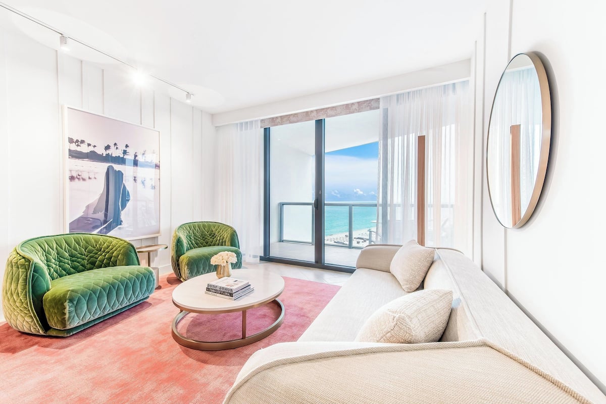 A modern living room with a green sofa, a white sofa, and a round coffee table. There is a large window with a view of the ocean.