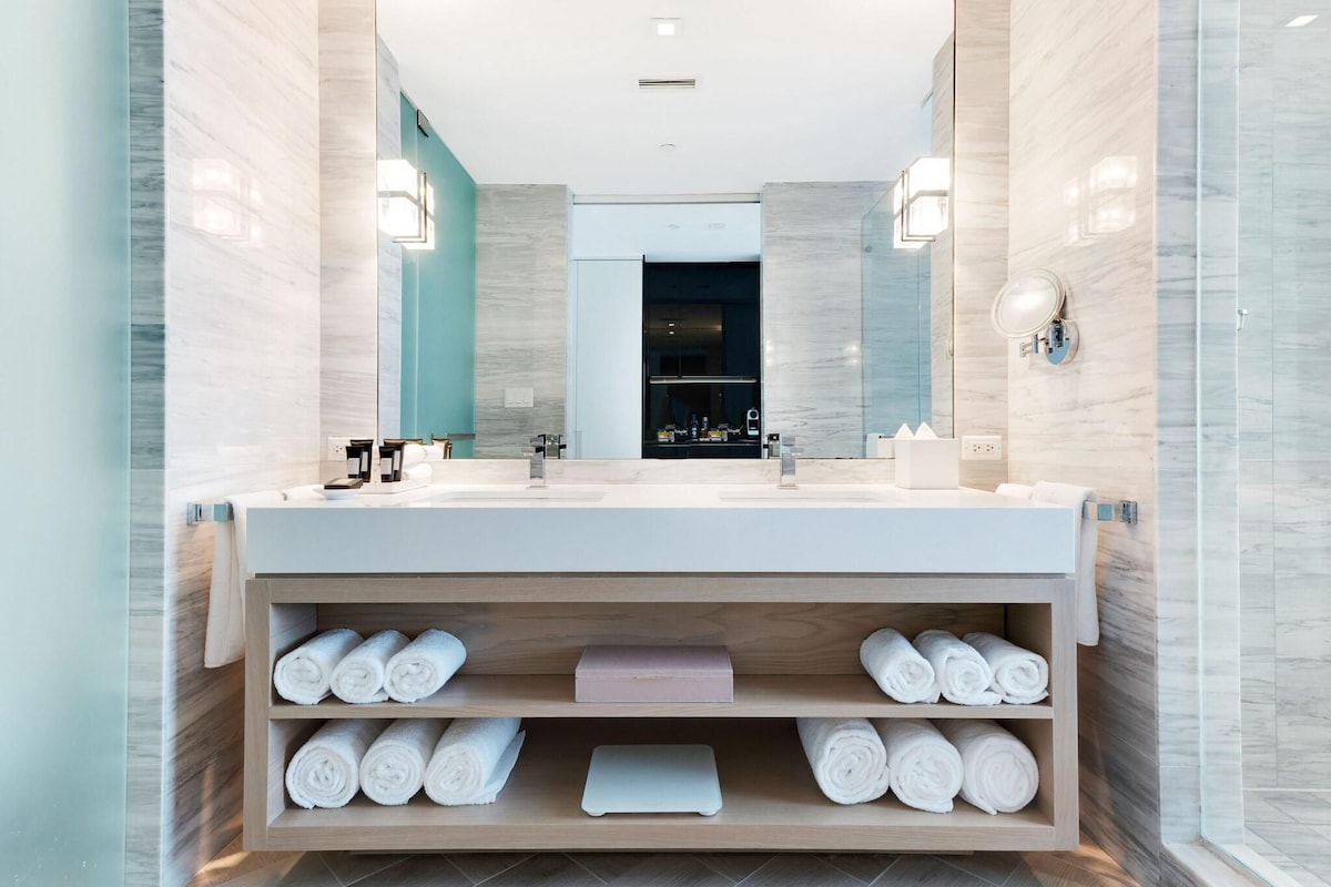 A modern bathroom with a double sink, built-in shelves for towels, and a large mirror.