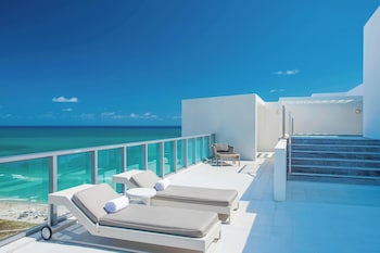 A modern interior with a large window offering a view of the sea, a dining area with a table and chairs, and a kitchen with white cabinets and a flat-screen TV. at W South Beach