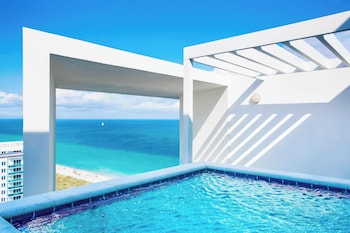 A room with a large window overlooking a beach, a small table with a vase, and a lamp on a side table. at W South Beach