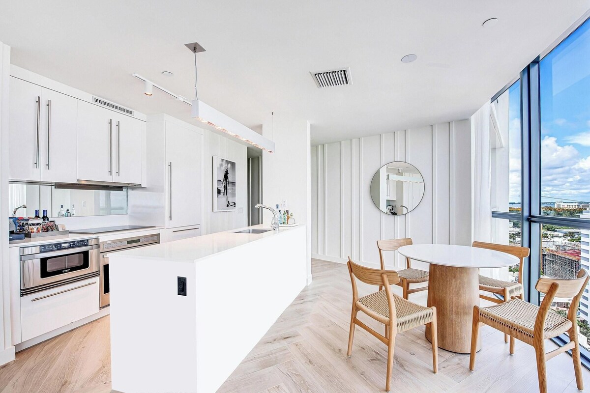 A modern kitchen with white cabinetry, a central island, and a dining area with a round table and wicker chairs.