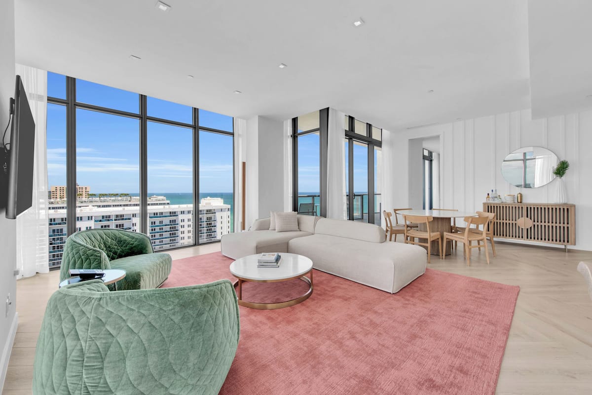 A modern living room with a large window, a sofa, a coffee table, and a dining area.