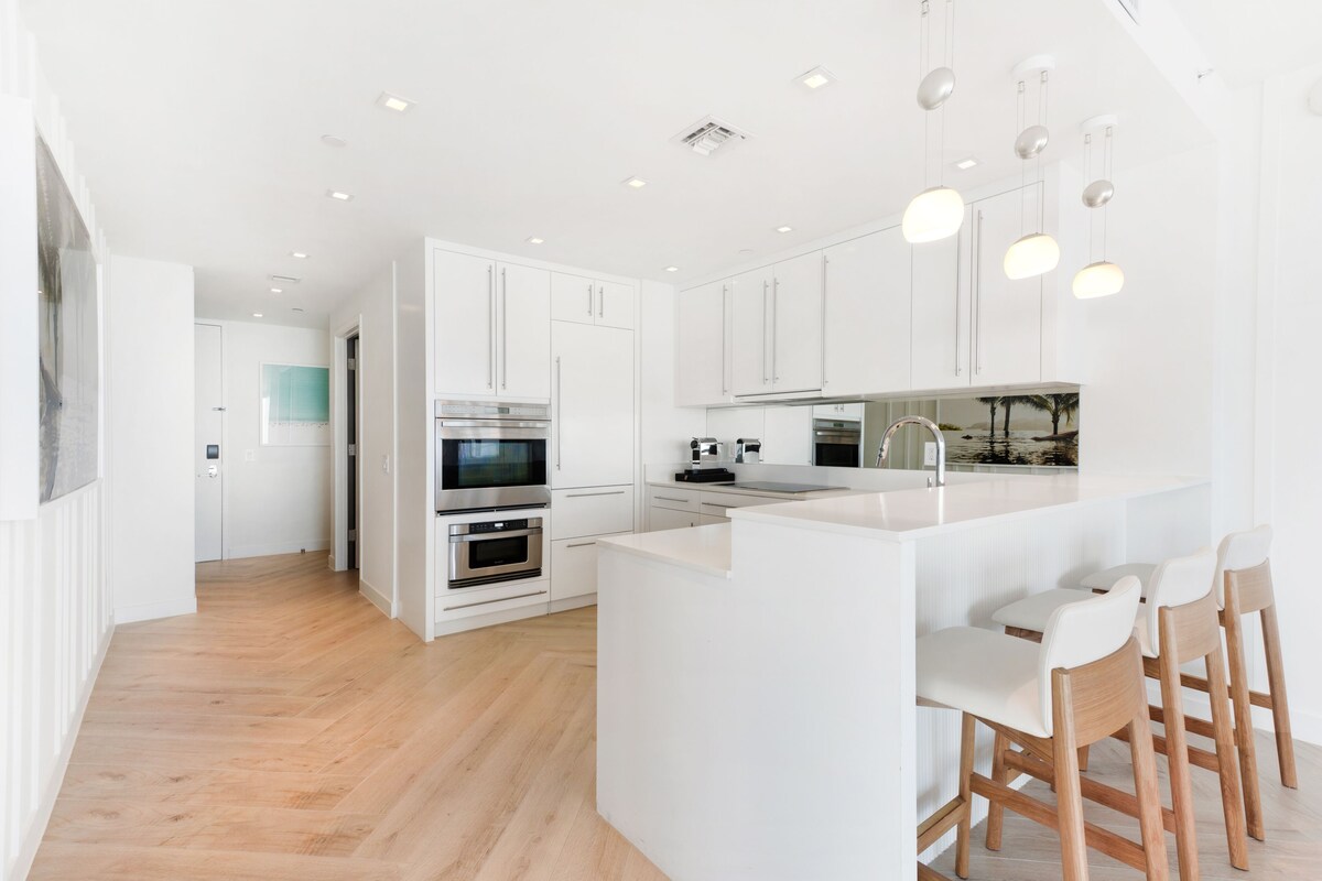 A modern kitchen with white cabinetry, a central island with bar stools, and built-in appliances.