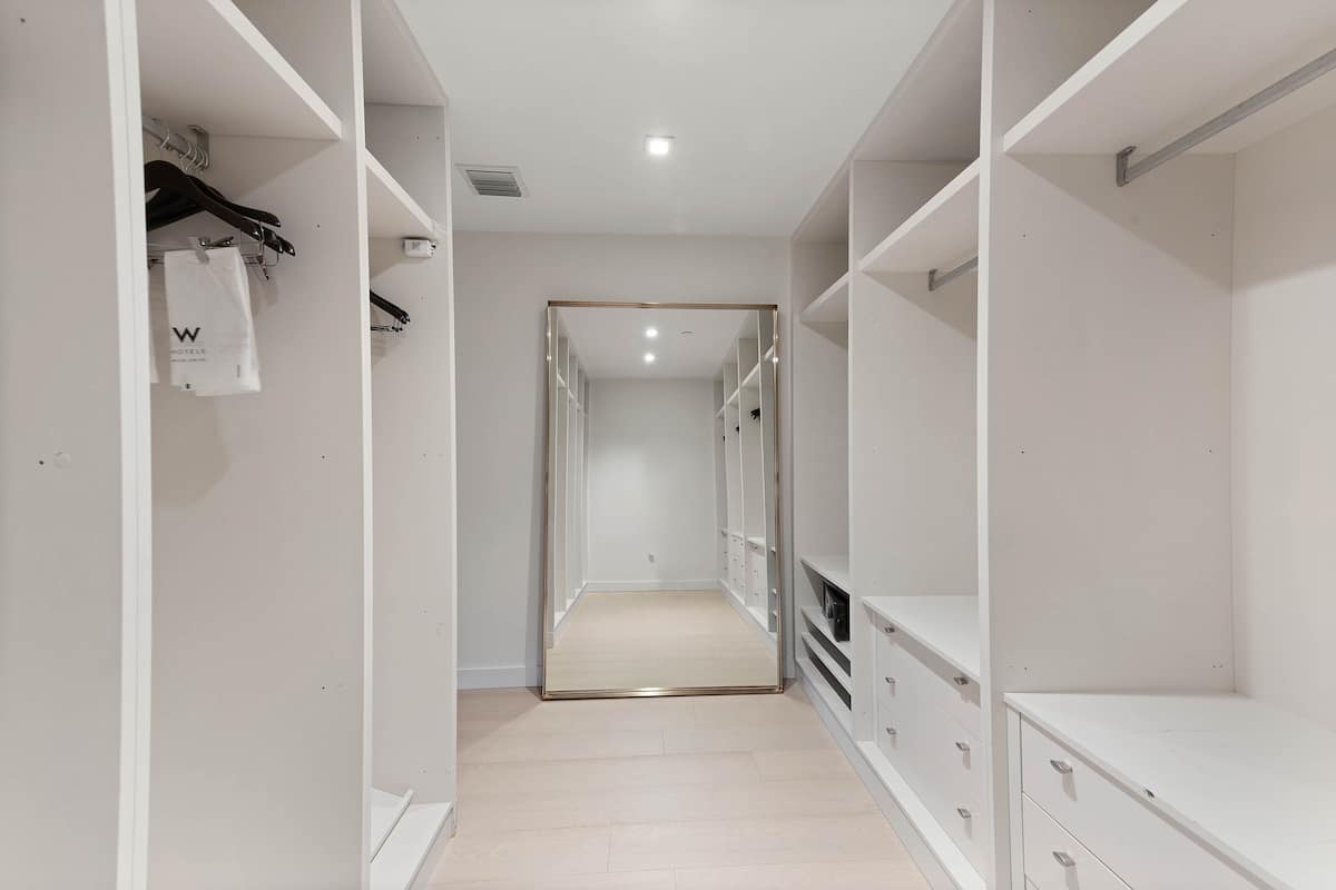 A hotel corridor with white walls, a wooden floor, and a mirrored closet door.