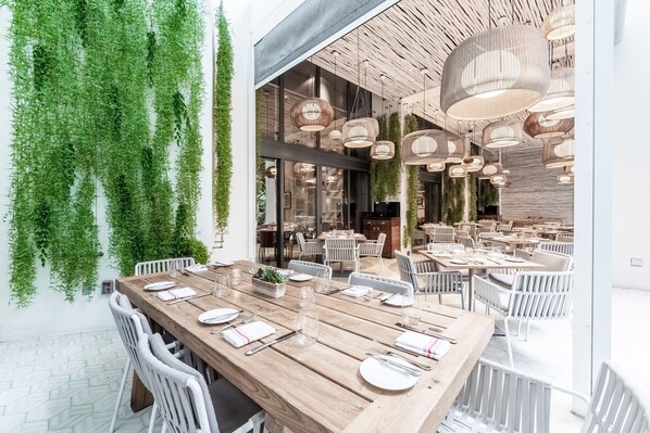 A modern dining area with wooden tables and white chairs, surrounded by hanging greenery and stylish pendant lights. - W South Beach (Miami Beach)