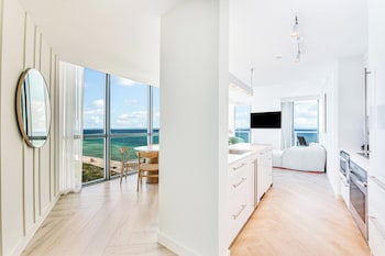 A modern lounge area with leather sofas, a bar with a variety of bottles, and large windows offering views of palm trees. at W South Beach