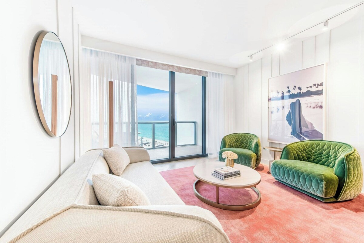 A modern living room with a large window, a green sofa, a white sofa, and a round coffee table.