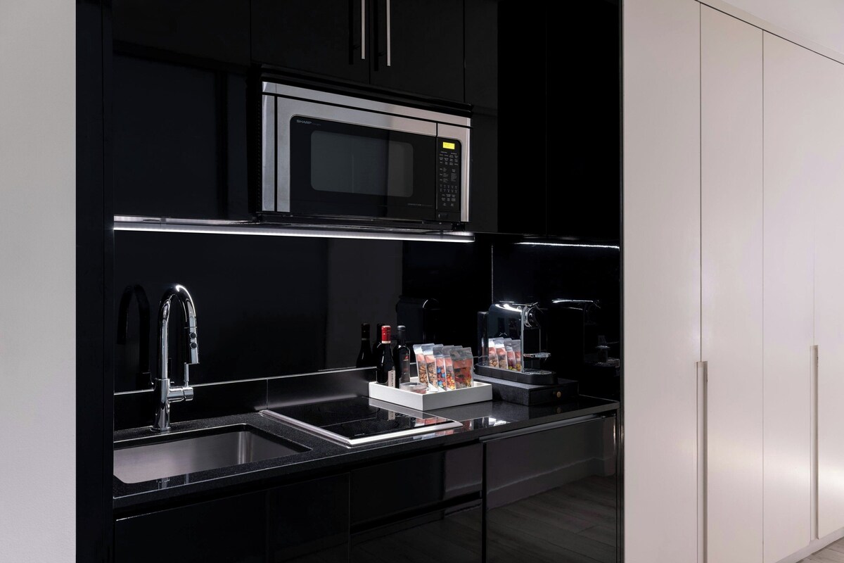 A modern kitchen with a black countertop, stainless steel sink, and a built-in microwave.