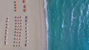 An aerial view of a beach with rows of beach umbrellas and lounge chairs arranged in a linear fashion along the shoreline. - W South Beach (Miami Beach)