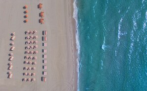 An aerial view of a beach with rows of beach umbrellas and lounge chairs arranged in a linear fashion along the shoreline. - W South Beach (Miami Beach)