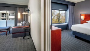 Une chambre d’hôtel comprenant un lit, un coin salon avec un canapé et un fauteuil, une petite table et une vue sur l’extérieur par une fenêtre.