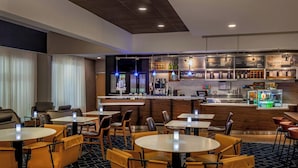 Un hall d’hôtel avec des tables et des chaises rondes, un coin bar et un espace dédié au café.