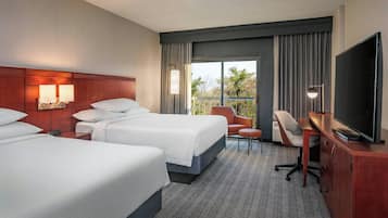 A hotel room with two beds, a desk, a chair, a TV, and a balcony with curtains.