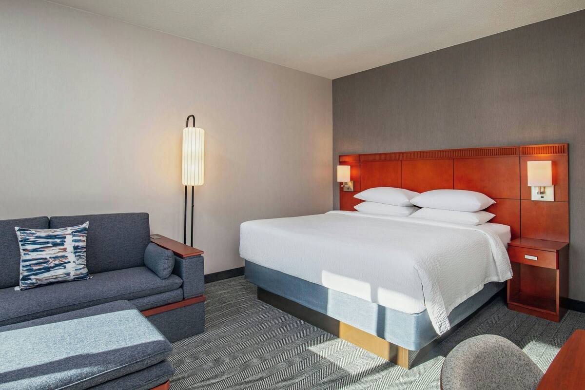 A hotel room with a bed, a sofa, a nightstand, and a lamp.
