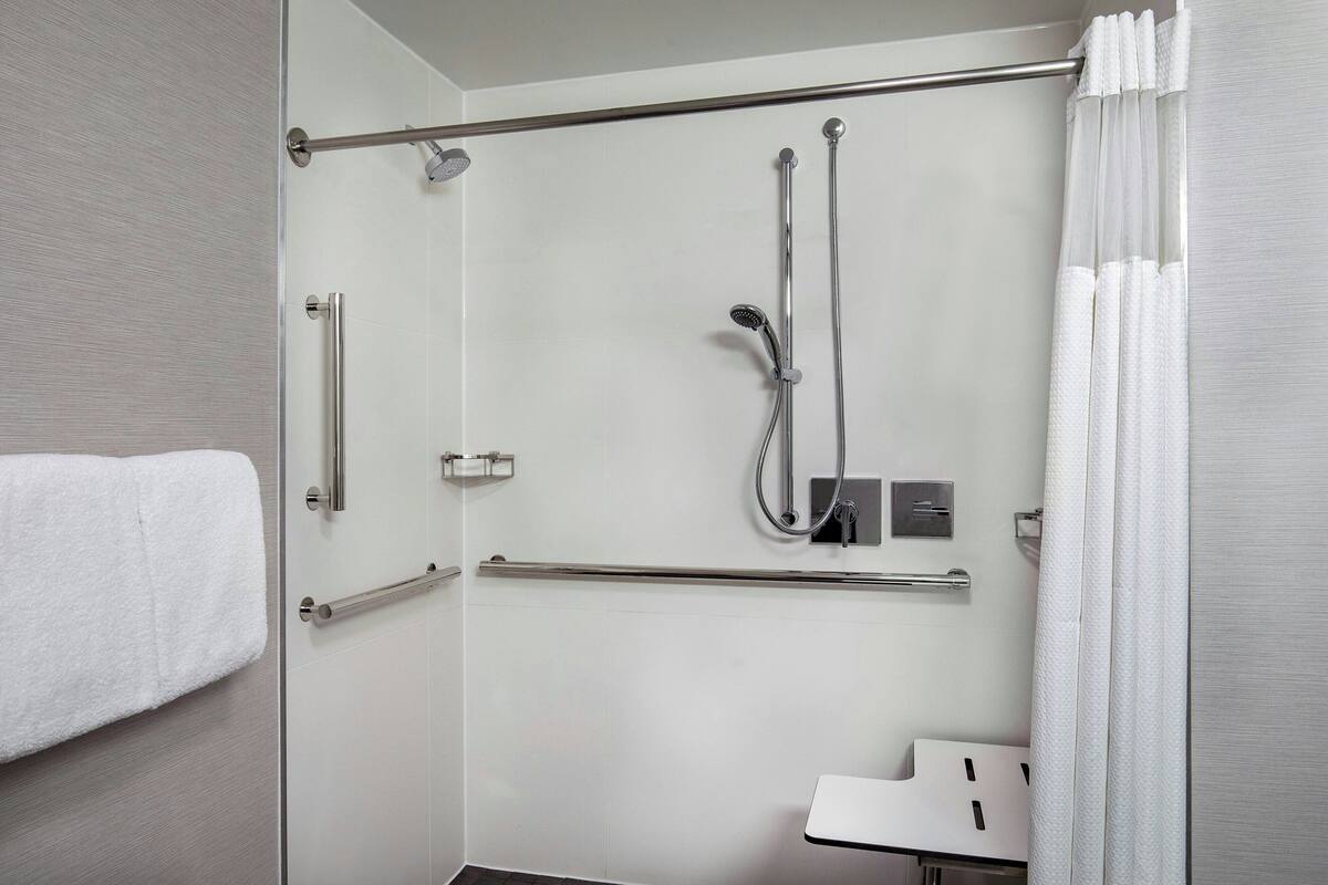 A modern bathroom with a glass shower enclosure, grab bars, a towel rack, and a white sink.