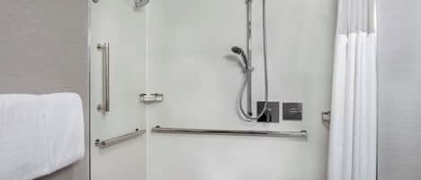 Une salle de bain moderne avec une douche à parois de verre, des barres d’appui, un porte-serviettes et un lavabo blanc.