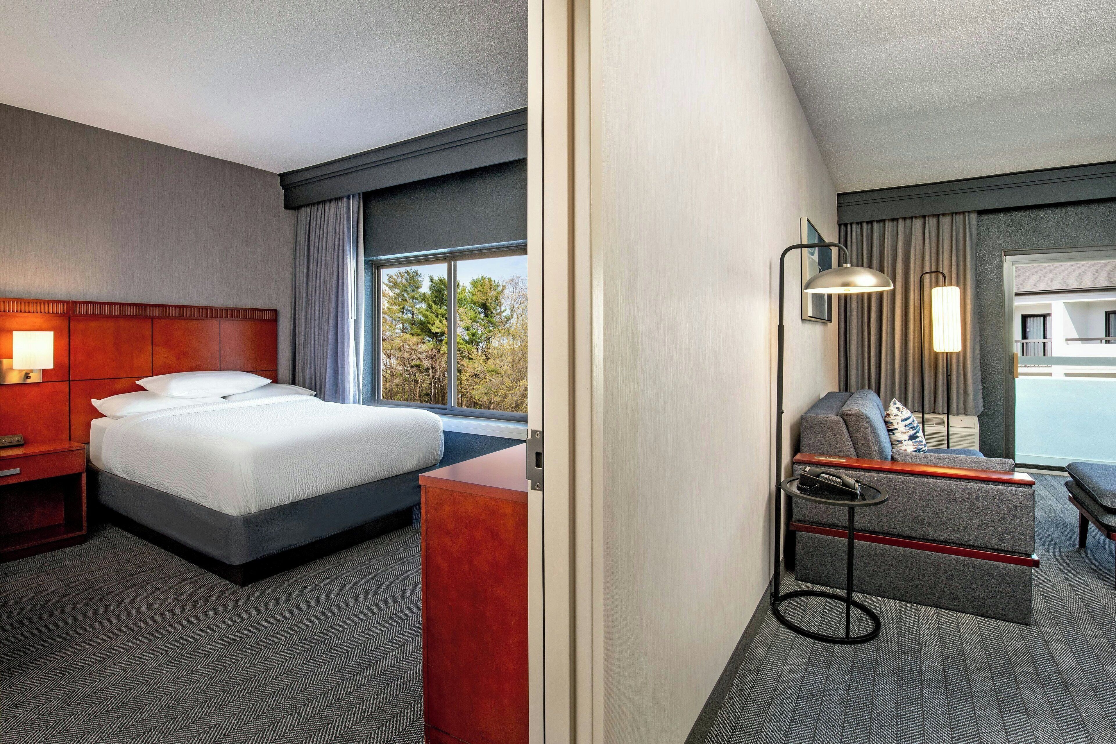 A hotel room with a bed, a desk, a sofa, and a window with a view of trees.