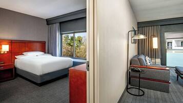 A hotel room with a bed, a desk, a sofa, and a window with a view of trees.
