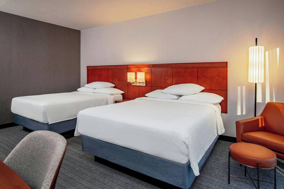 A hotel room with two beds, a sofa, a chair, and a lamp.