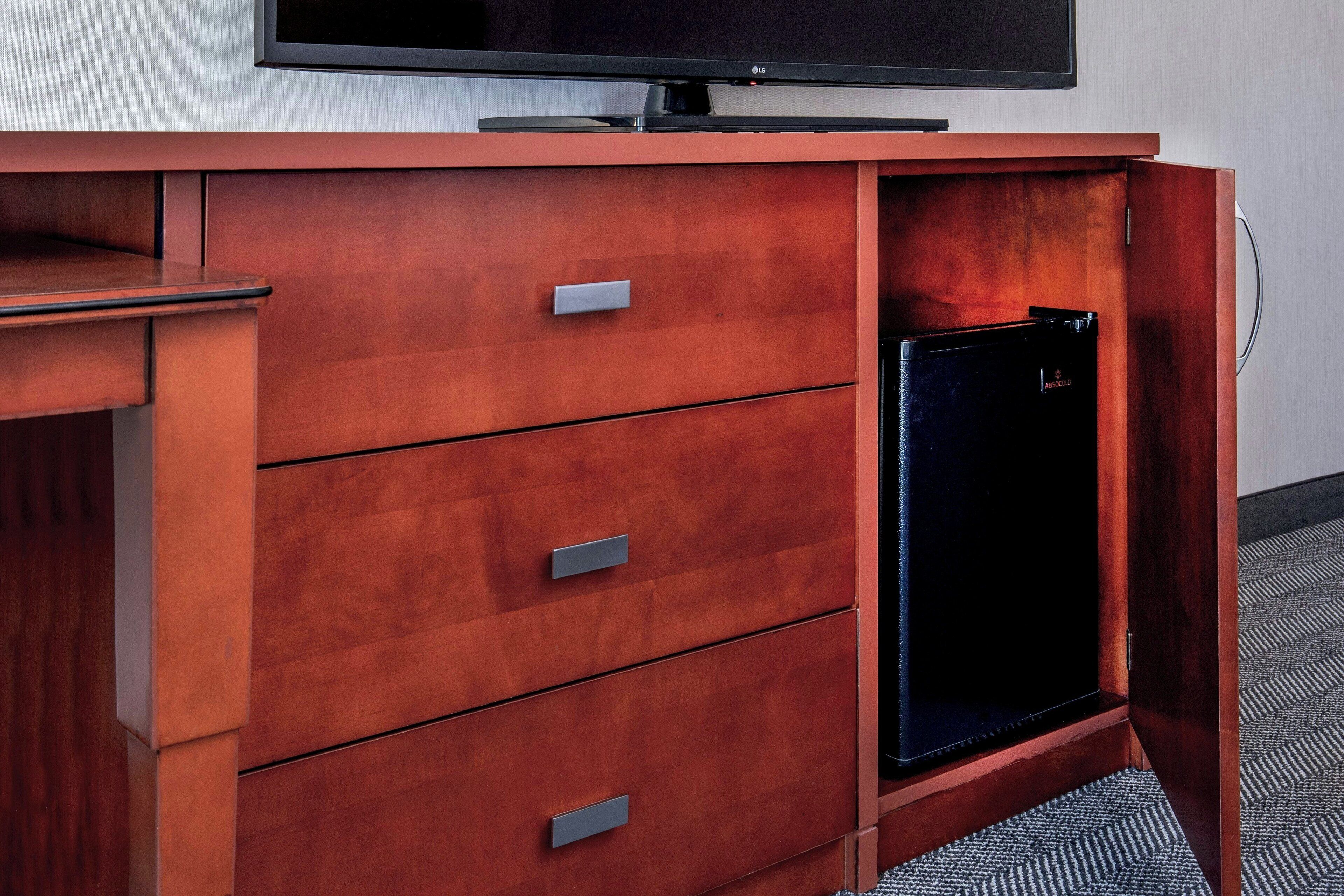 A wooden cabinet with a flat-screen TV on top and a small black refrigerator built into the cabinet.