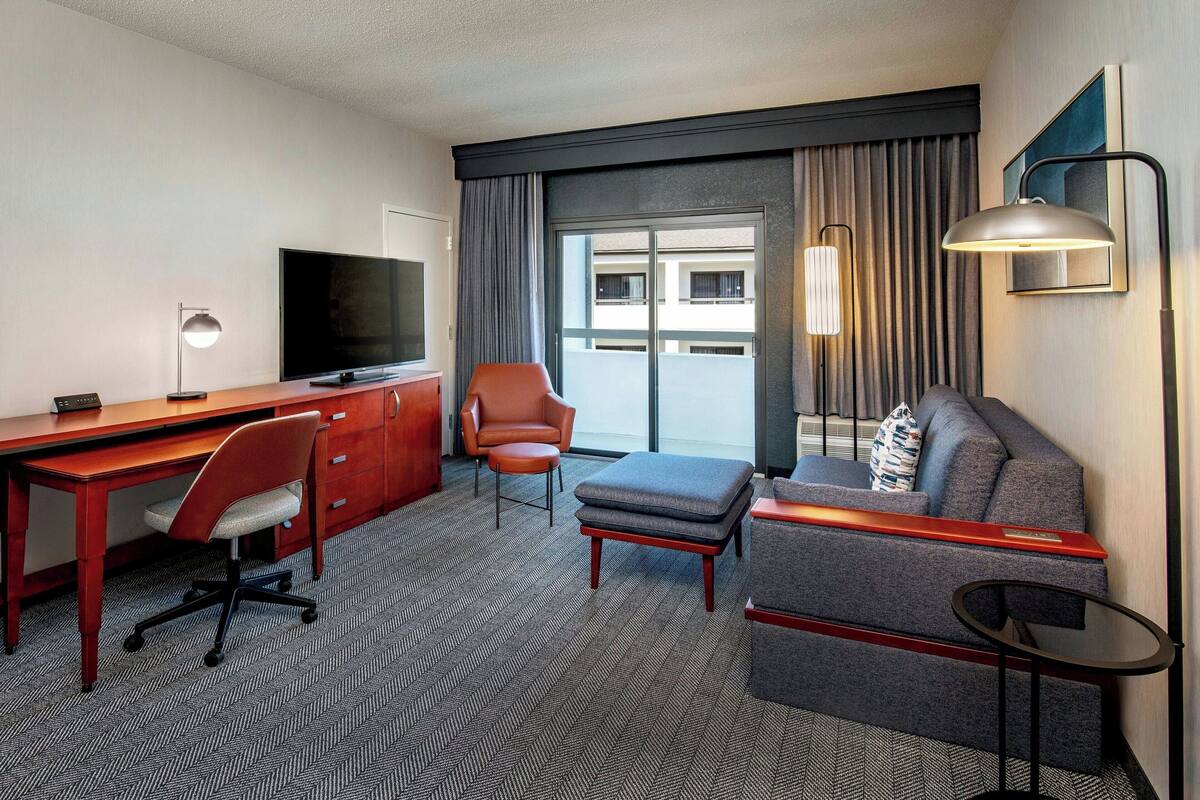 A hotel room with a desk, television, and seating area.