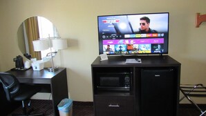 A hotel room with a television displaying a movie, a desk with a lamp, a chair, a trash bin, and a minibar. - Super 8 by Wyndham New Cumberland (New Cumberland)