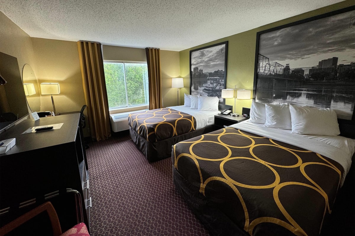 Une chambre d’hôtel avec deux lits, un bureau, une chaise, une fenêtre avec des rideaux et deux lampes.