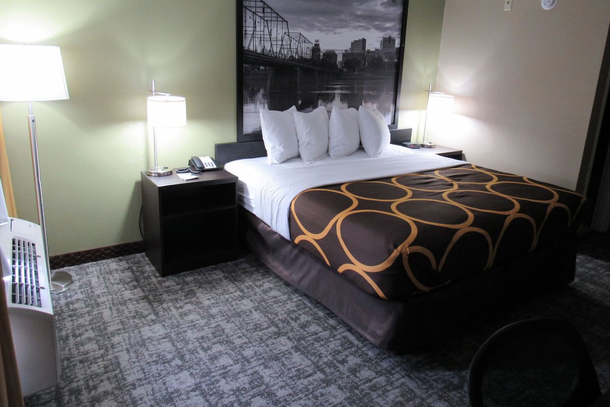 Une chambre d’hôtel avec un lit, deux tables de chevet, un bureau, une chaise, une lampe et un grand tableau représentant un paysage urbain accroché au mur.