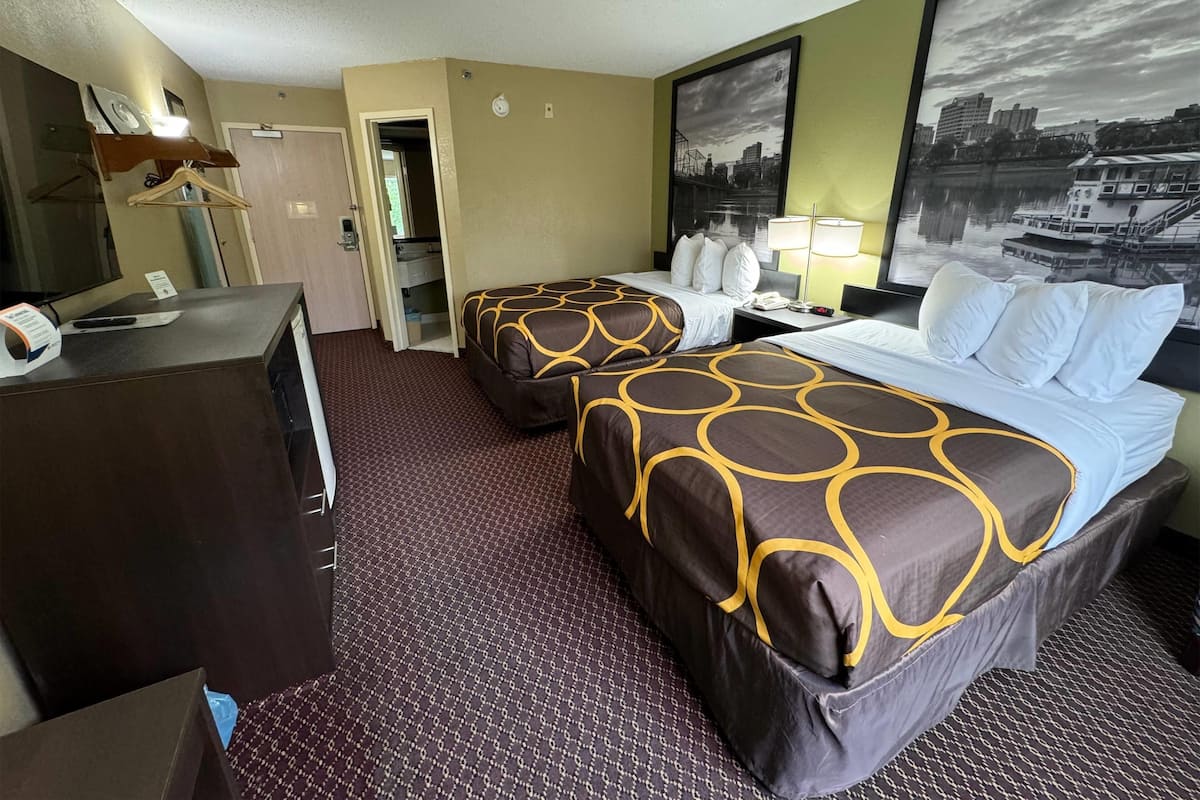 Une chambre d’hôtel avec deux lits, un bureau, un miroir et une grande fenêtre donnant sur le paysage urbain.