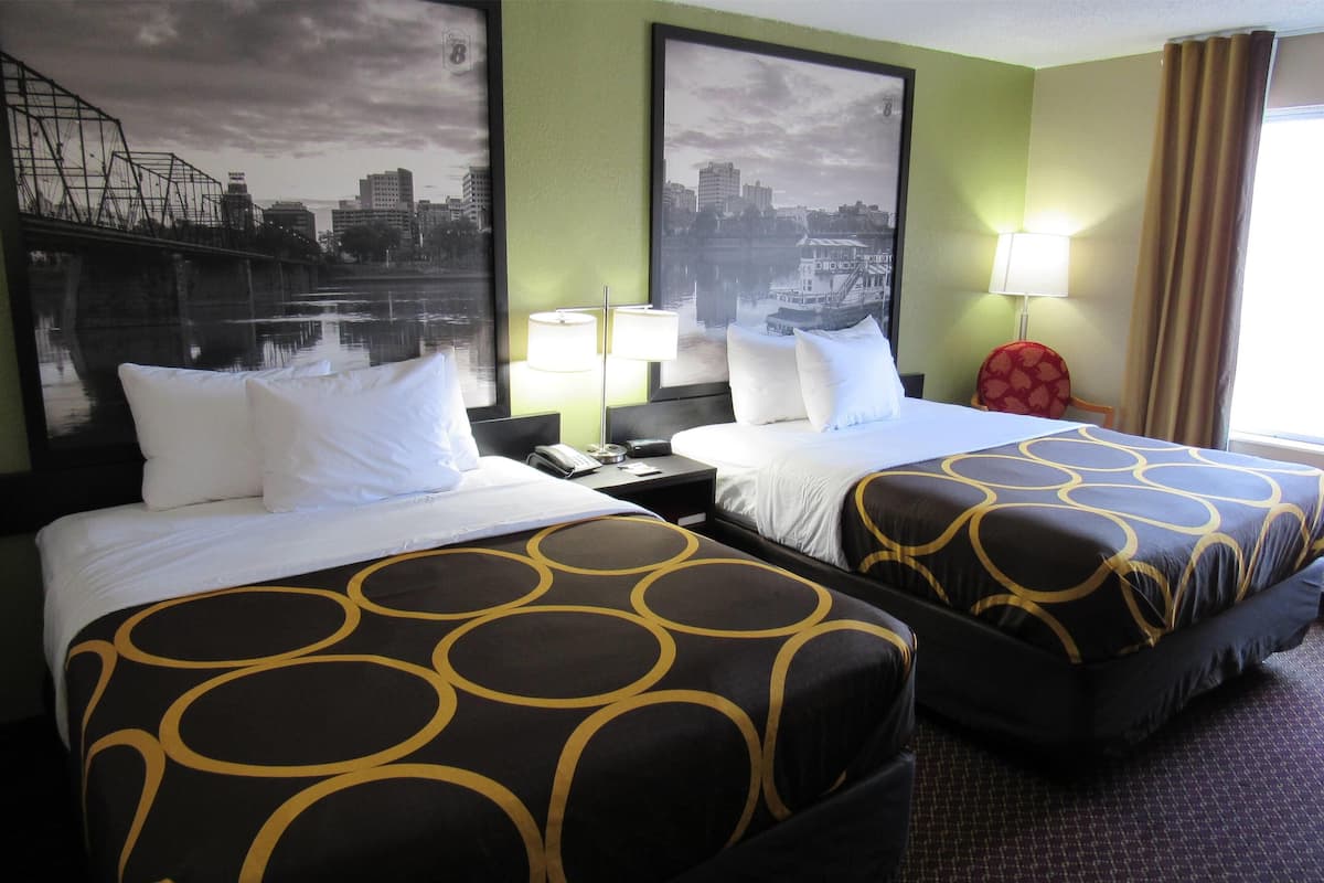 Une chambre d’hôtel avec deux lits, une vue sur la ville, un fauteuil rouge et une table de chevet avec une lampe.