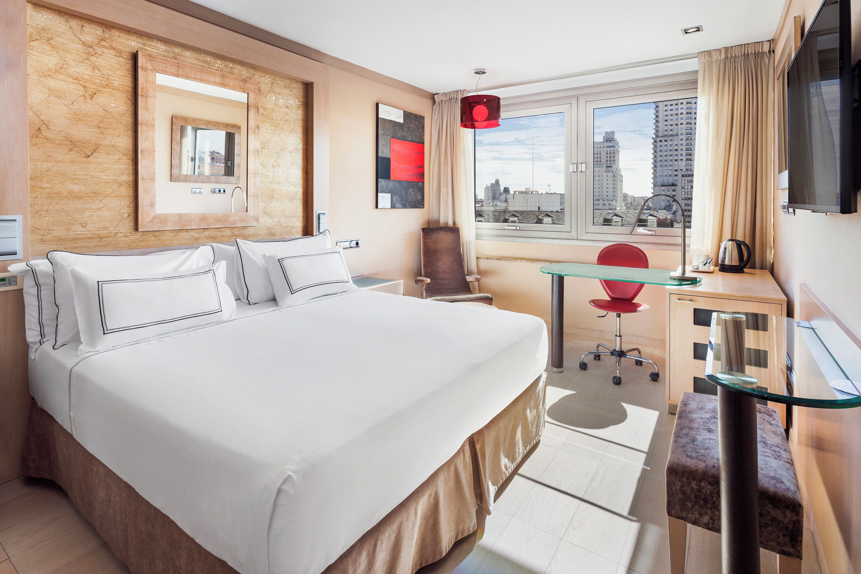 Habitación de hotel con una cama grande, un escritorio con silla, televisión y vista a la ciudad.