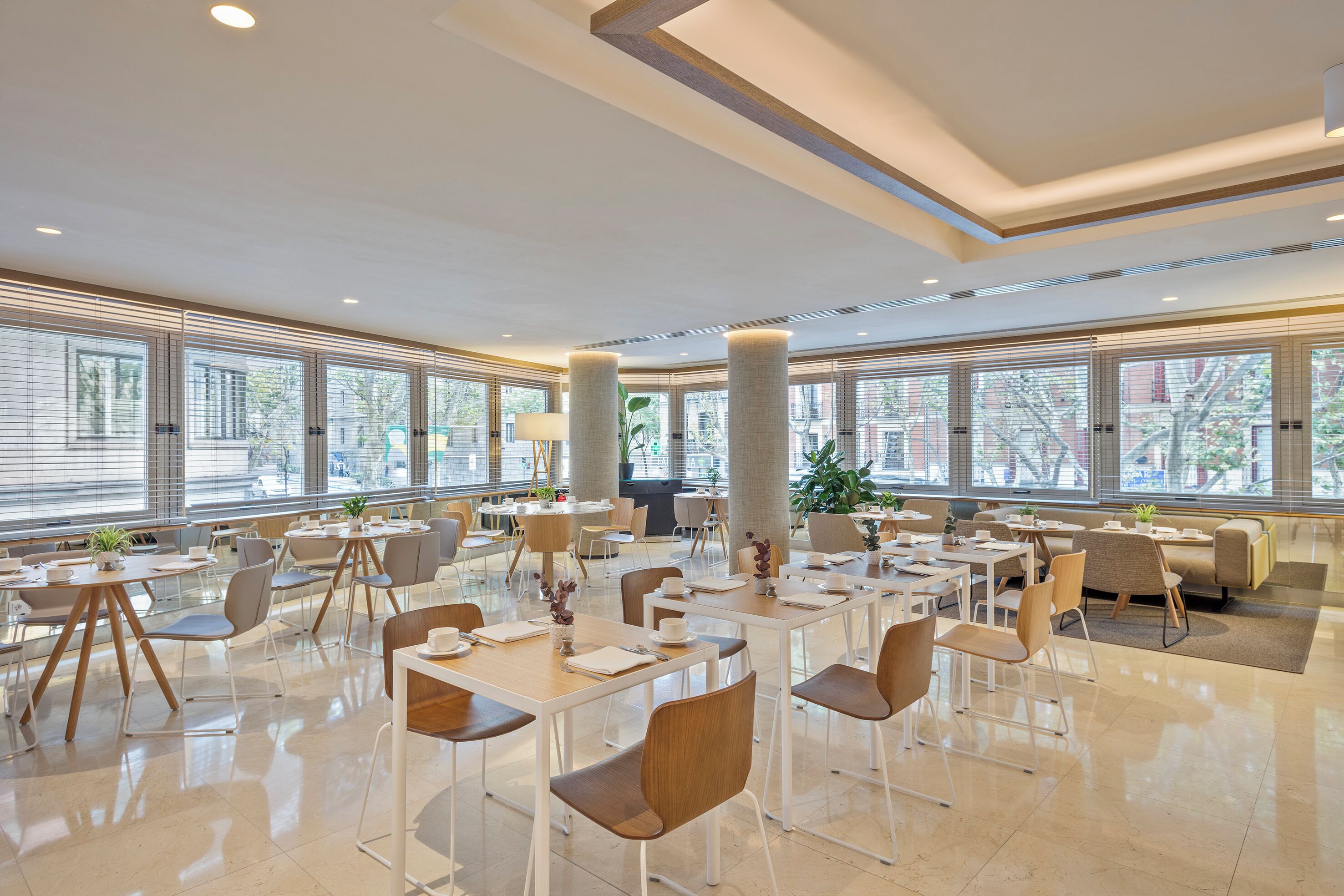 Un comedor amplio con varias mesas y sillas, ventanas grandes y un diseño de techo moderno.