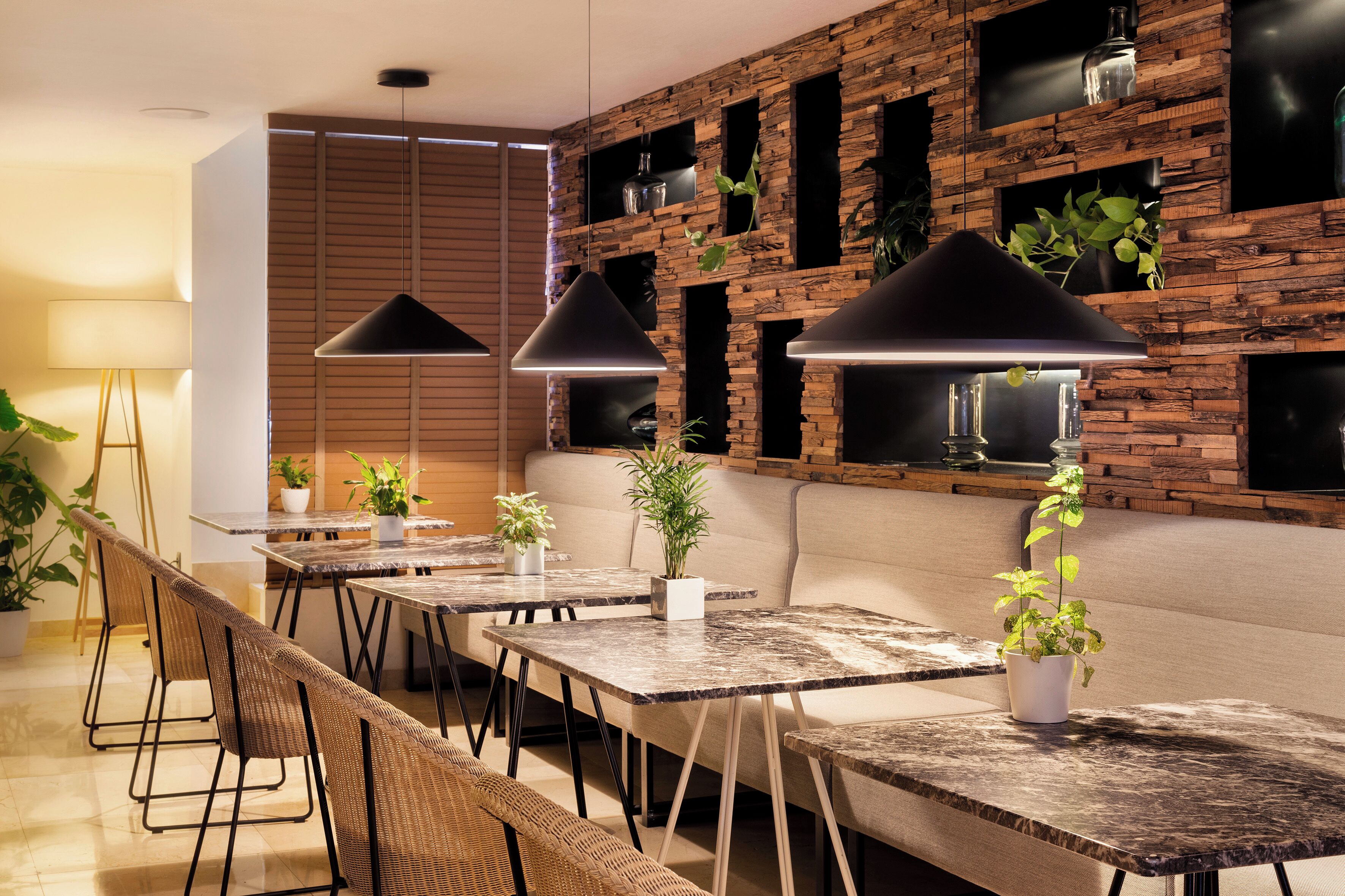 Un comedor moderno con paredes de madera, lámparas colgantes negras y plantas en macetas.